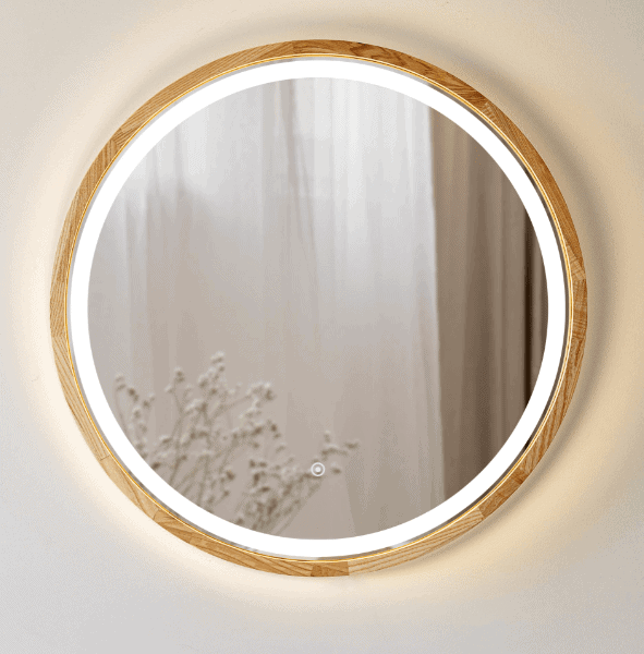 Pitagoras-Perfection-Slim-LED4.png to okrągłe lustro ścienne z drewnianą ramą i wbudowanym oświetleniem LED, odbijające przezroczyste zasłony i mały bukiet białych kwiatów w delikatnie oświetlonym pomieszczeniu.