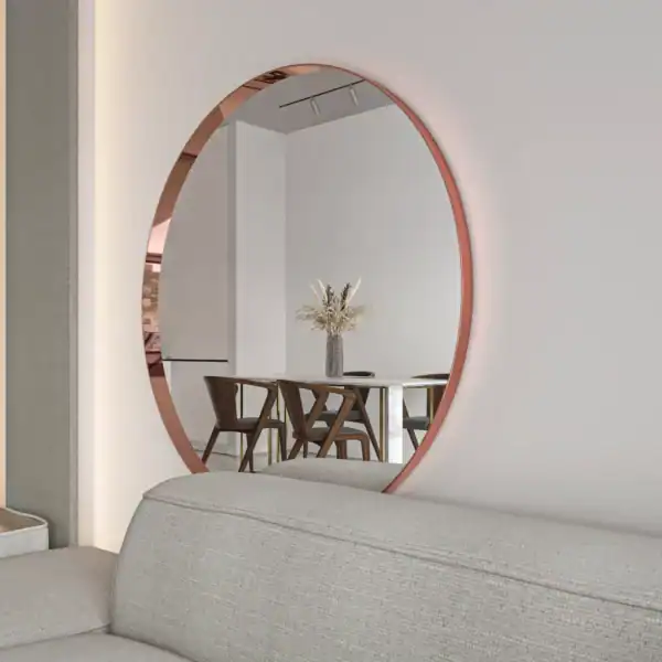 Okrągłe lustro miedz_closeup-scaled-1.webp nad jasnoszarą sofą odbija stół z drewnianymi krzesłami i wazon z suszonymi kwiatami, tworząc nowoczesną, minimalistyczną scenę wnętrza.